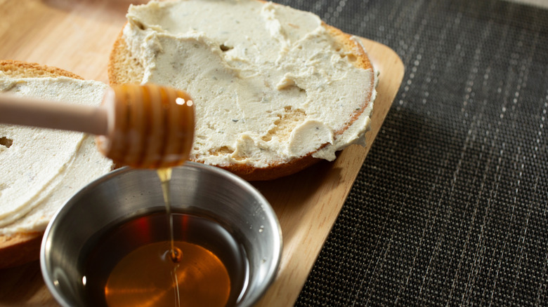 Honey dipper, stainless steel cup with honey, and bagel with cream cheese