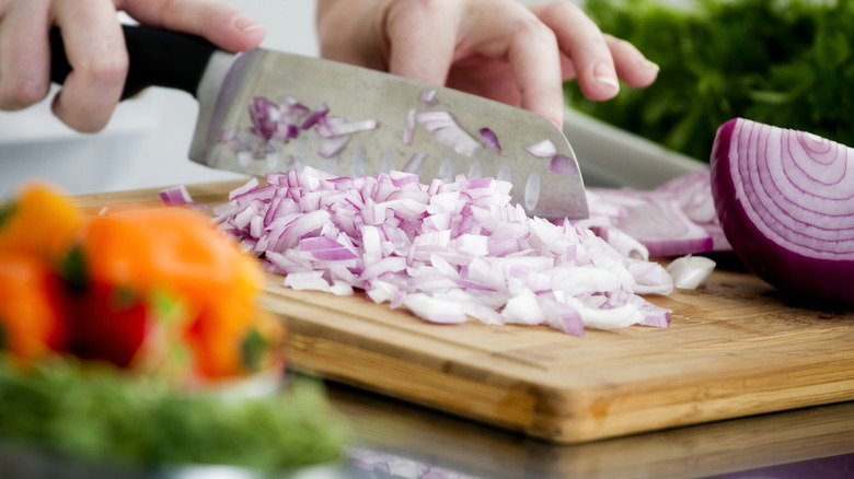 caucasion hands chopping red onion on wooden cutting board