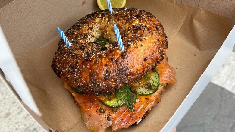 Bagel with lox, dill, pickles, and capers in box with 3 blue birthday candles in the top