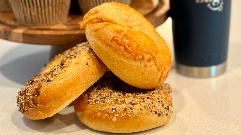 Three bagels on counter with muffins and travel mug blurred in background