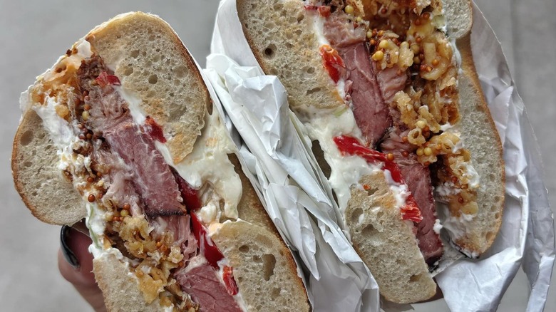 Hand holding two halves of bagel with brisket and cream cheese