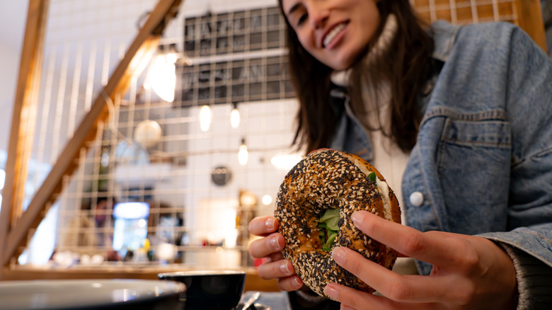 Woman sitting at table in cafe holding bagel and smiling