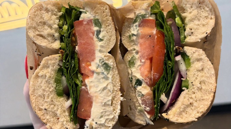 Two halves of a bagel with tomato, spinach, and cream cheese