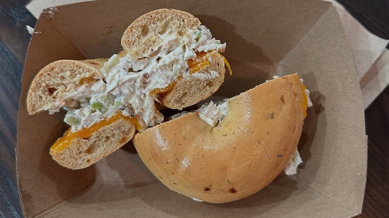 Chicken salad bagel sandwich cut in half from above and from the side, in cardboard tray