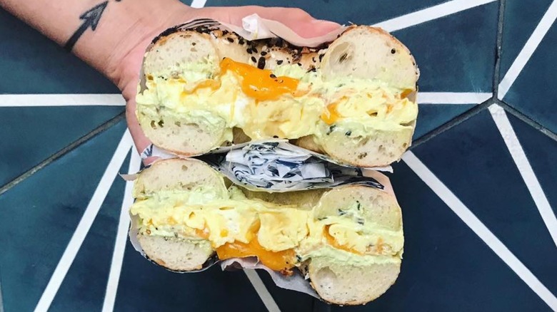 Hand holding two halves of a bagel sandwich cut open to reveal eggs and cheese.
