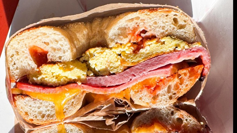Bagel sandwich cut in half to reveal eggs, ham, and melted cheese.