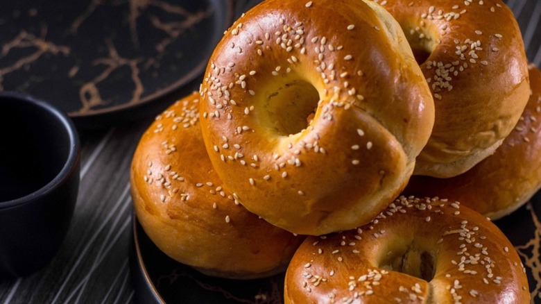 Pile of seeded bagels on black plate and black table