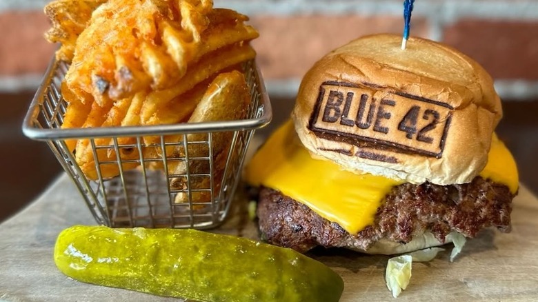 A cheeseburger with fries and a pickle from Blue 42.