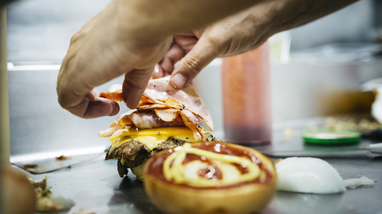 A chef assembles a cheeseburger on the griddle.