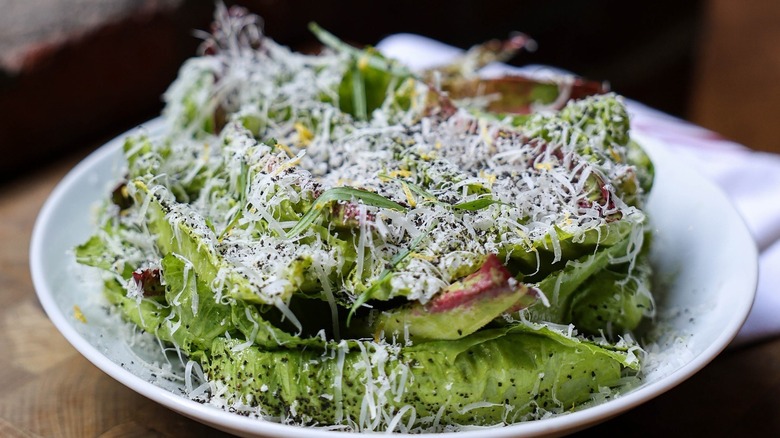 Caesar salad topped with shredded Parmigiano Reggiano and squid ink breadcrumbs on a white plate