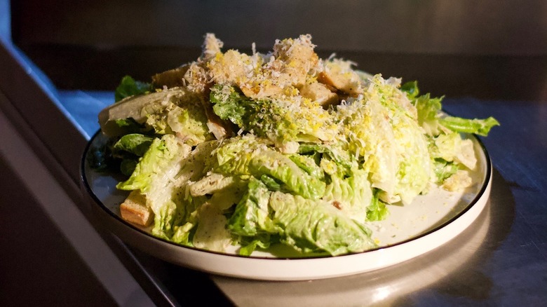 A Caesar salad on a white plate under a spotlight