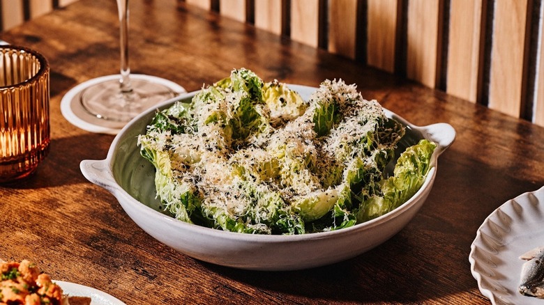 Caesar salad in a white bowl on a wooden table with wine glass in the background