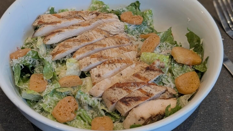 A Caesar salad topped with grilled chicken and round croutons