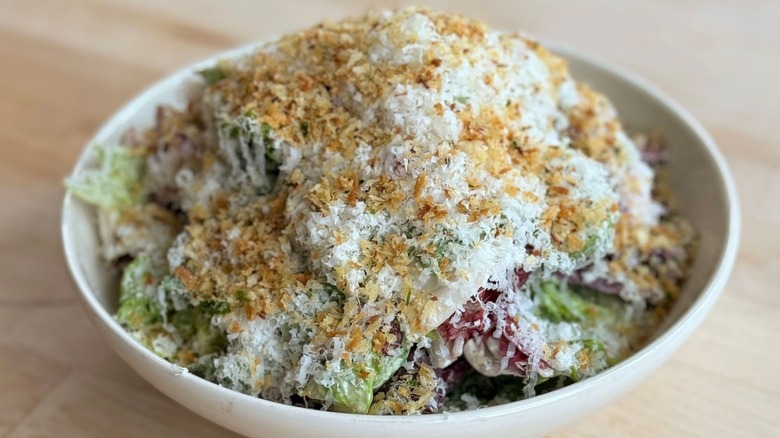 A Caesar salad topped with a generous amount of grated cheese and breadcrumbs in a white bowl