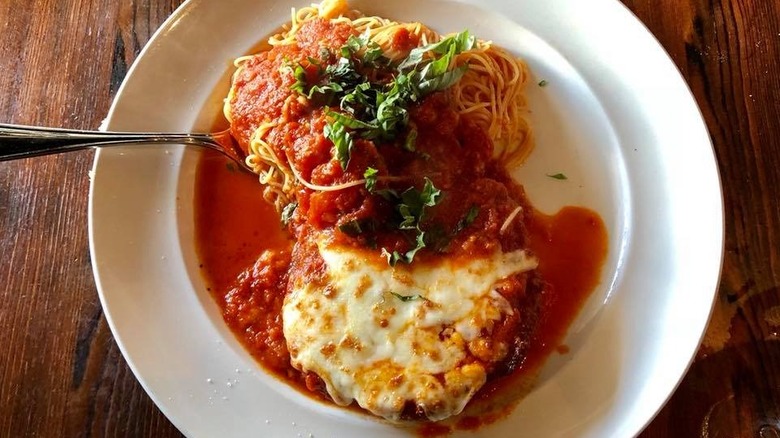 A plate of chicken parm on a wooden table with a fork in it