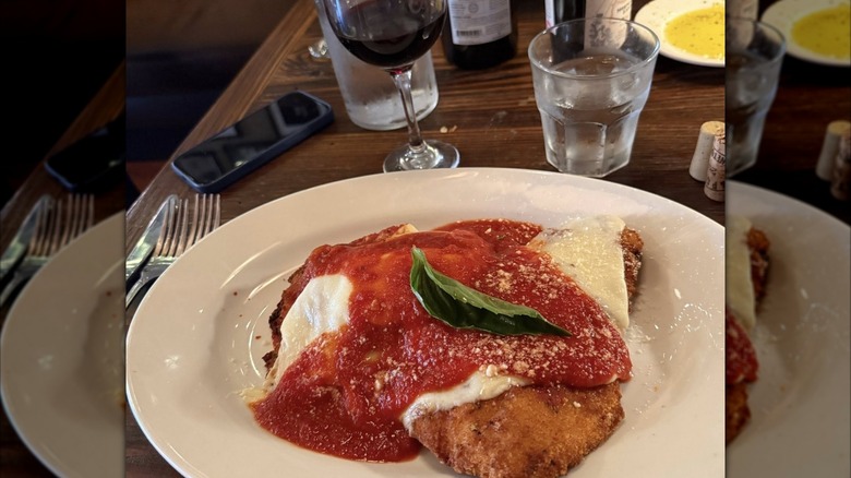 Spano's chicken parm on a table with a glass of water and a glass of red wine