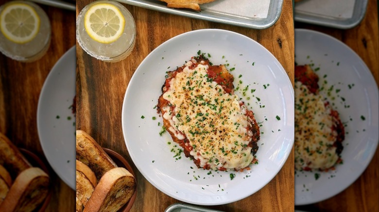 Chicken parm from Dovetail on a plate with a glass of lemon water in the background