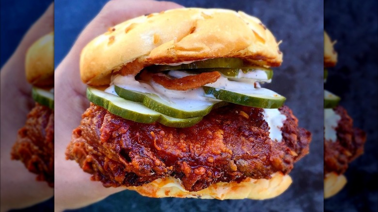 A hand holding Crack Shack's Firebird sandwich that's filled with pickles, ranch, and juicy, fiery chicken.