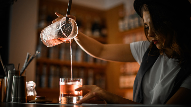 Female bartender pours pink cocktail from shaker