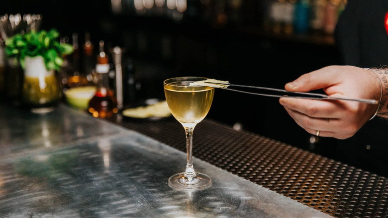 Bartender garnishes a cocktail using tweezers