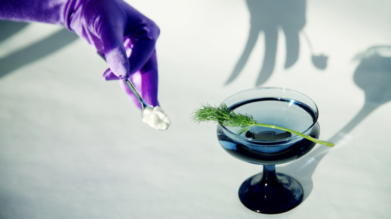 A purple-gloved hand garnishes a cocktail