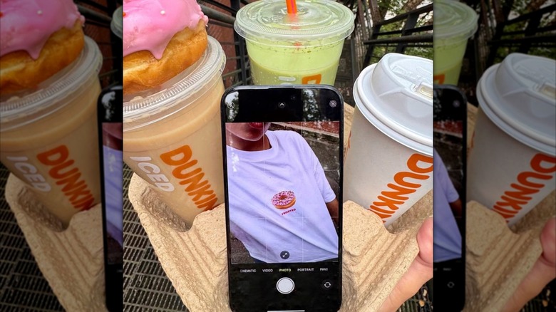Urban Outfitters t-shirt reflected in iphone propped up against various Dunkin' coffee drinks.