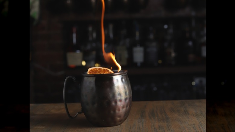 A goblet with an orange slice on top and fire coming from the top