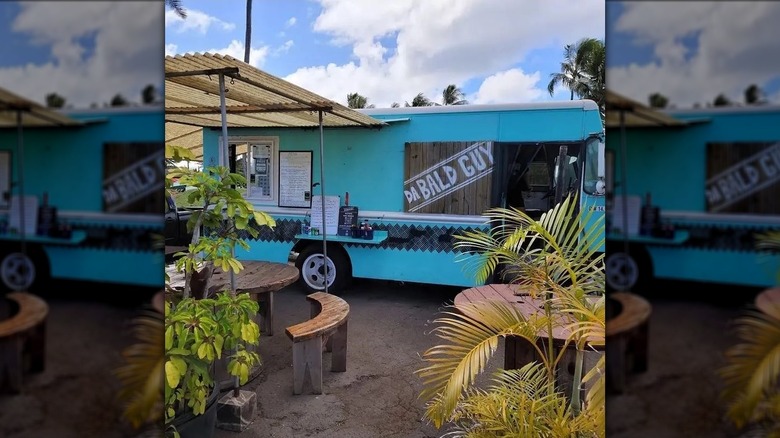 The blue exterior of Da Bald Guy food truck with greenery and tables outside