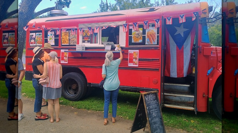 A line of customers at Wehpah food truck, located in a red school bus