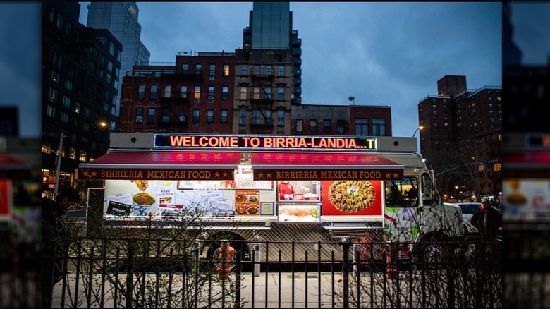 Exterior of Birria-Landia at dusk with New York City buildings in the background