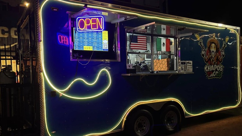 Exterior of the Chapos Tacos truck with a neon sign lit up at night