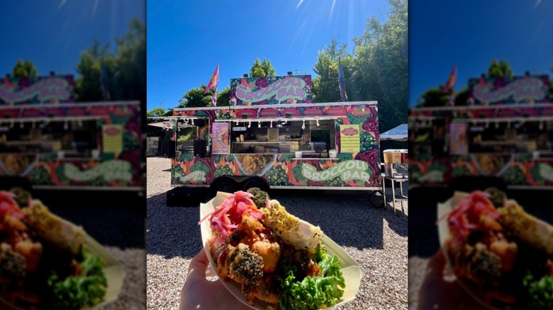 Hand holding a dish of food in front of The Broccoli Bar