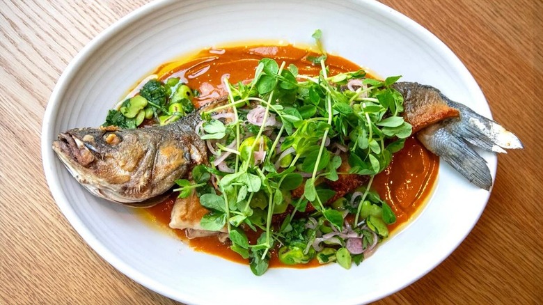 Whole roasted branzino in piri piri broth garnished with greens on an oval white plate at Avec
