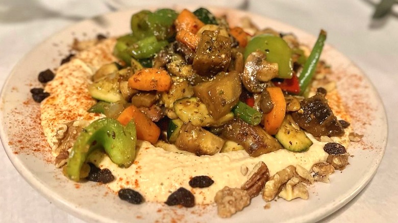 Turkish Delight dish of sautéed veggies on hummus with raisins and walnuts on a white plate at The Bosphorus Istanbul Cafe