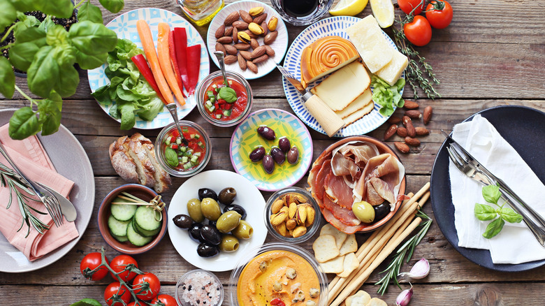 Mediterranean appetizers on assorted platters, including olives, nuts, hummus, cured meats, and cheeses