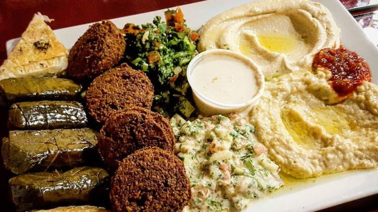 Appetizer sampler with stuffed grape leaves, falafel, tabbouli, hummus, baba ghannoush, and tahini sauce on a rectangular white plate at Holy Land Cafe