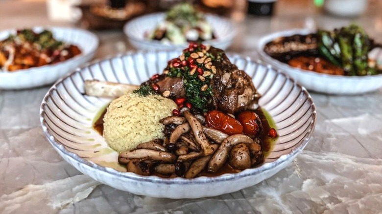 Braised lamb shank with a pine nut gremolata, pomegranate seeds, and rice on a black and white fluted plate at Ammoora