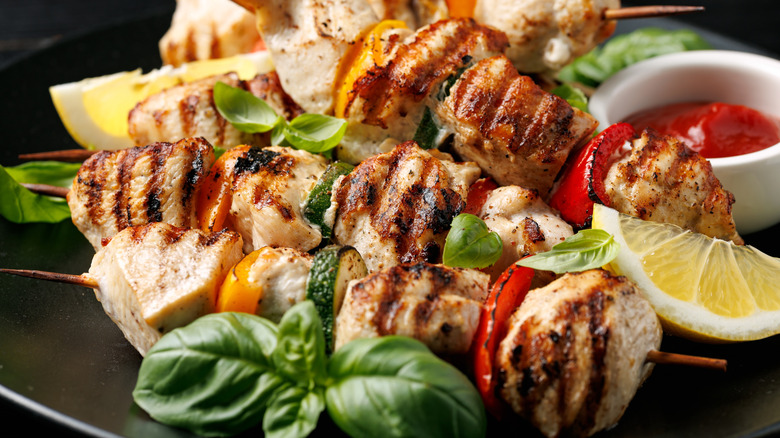 Close up of chicken kebabs garnished with lemon wedges and fresh basil