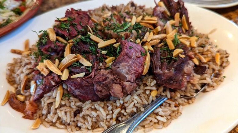 Stuffed lamb over rice, garnished with parsley and toasted almond slivers on a white plate at Al Ameer Restaurant