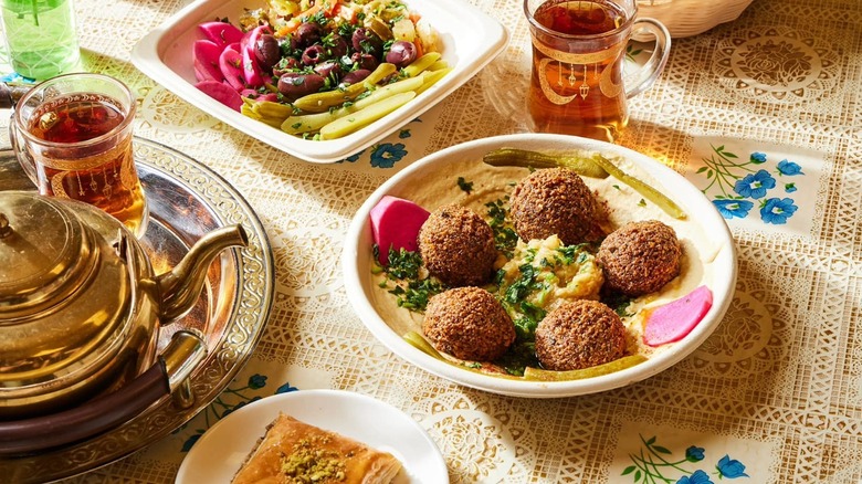 Plate of falafel with hummus, olives, baklava, and tea in a glass at Baba's Pantry