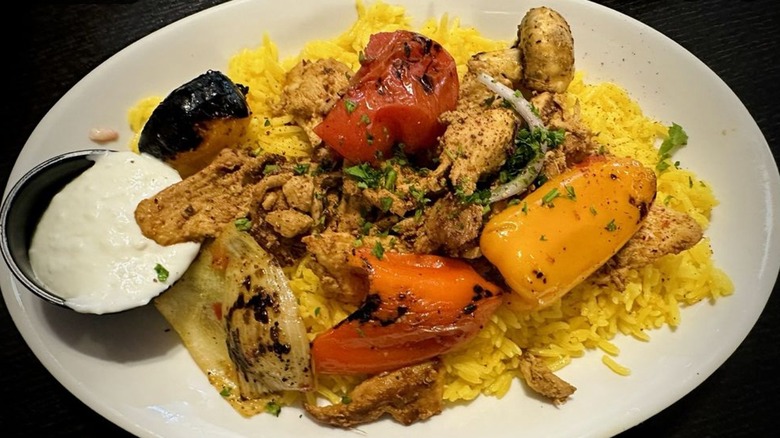 Chicken shawarma over rice with grilled vegetables and yogurt sauce on a white, oval plate at El Basha Grill & Catering