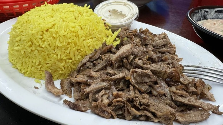 Lamb shawarma with rice and tahini sauce on a white, oval plate at Alquds Mediterranean Grill & Grocery