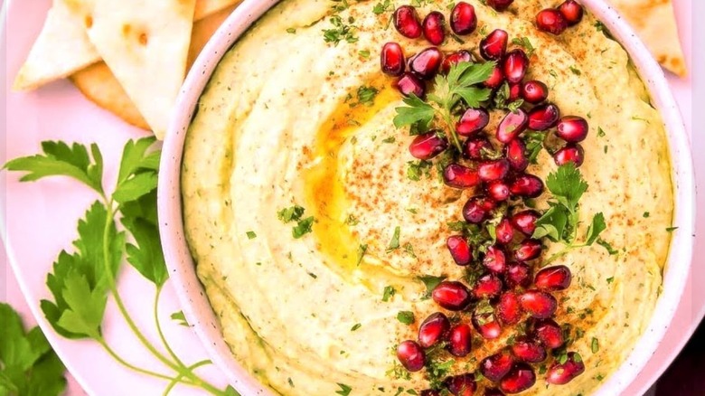 Pink bowl of hummus garnished with olive oil, parsley, and pomegranate seeds, served with pita at Cafe Aladdin