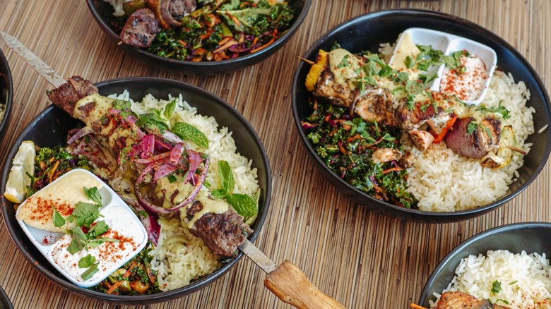 Black plates of kebabs with rice, salad, and dipping sauces at Nicholas Restaurant