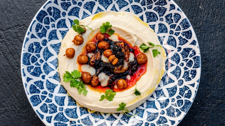 Decorative blue and white plate with hummus garnished with roasted chickpeas, chili oil, and parsley at Aba