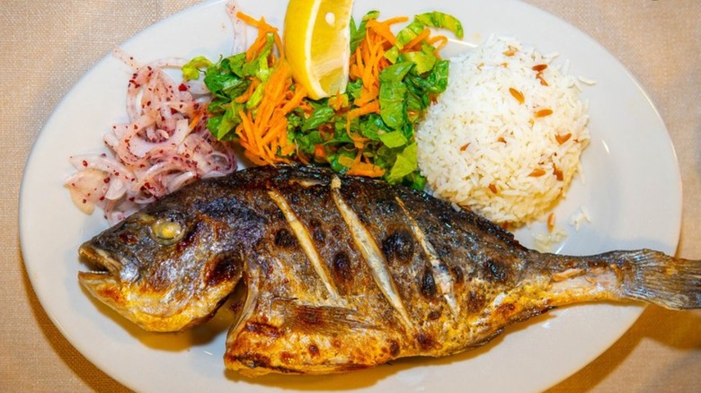 Whole grilled fish with rice, salad, pickled vegetables on an oval white plate at Kismet Mediterranean
