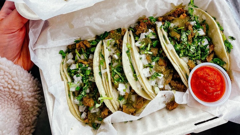 A person holding a takeout container of tacos from Cruz Tacos