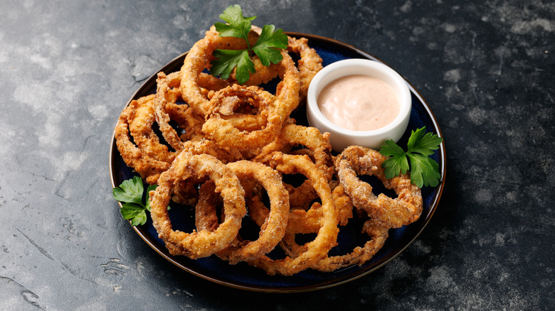 Onion rings on a black plate with dipping sauce