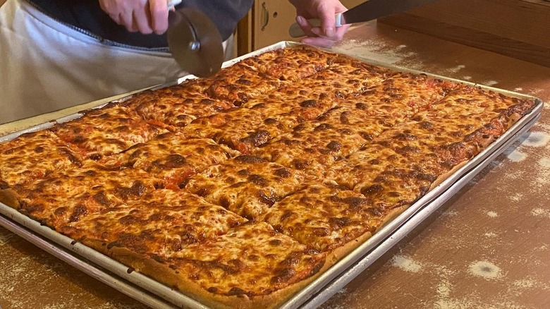 A person slicing a cheese pizza at Galleria Umberto