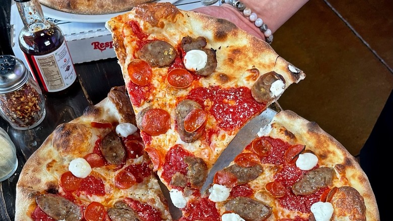 A person holding a slice of New Yorker pizza at Pizza Rock